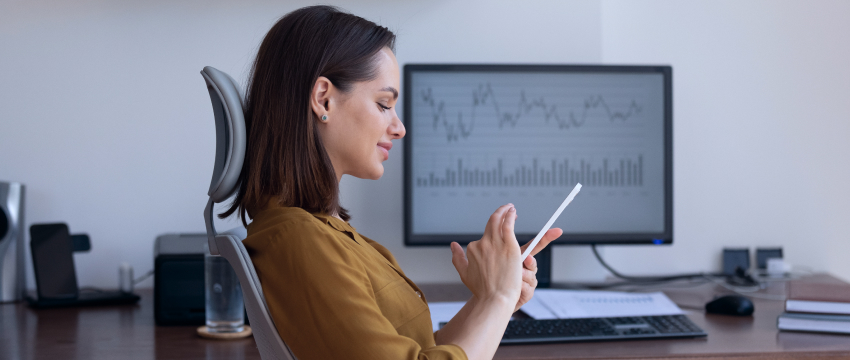 Uma mulher em sua mesa, usando um tablet, exemplificando uma trader fundamental em ação.