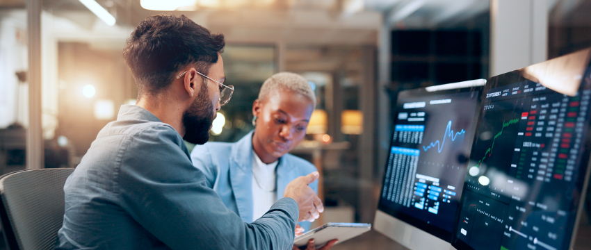 Two professional traders review financial data on computer screens in a modern office, with graphs and charts visible on the monitors with mt4 screenshots.