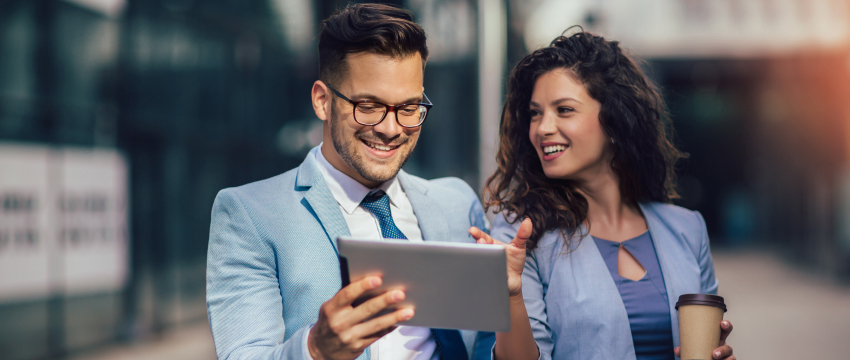 A man and woman in business attire are analyzing forex trading data on a tablet together.